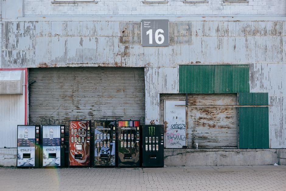 Rustic warehouse exterior featuring a row of vending machines outside a garage door.