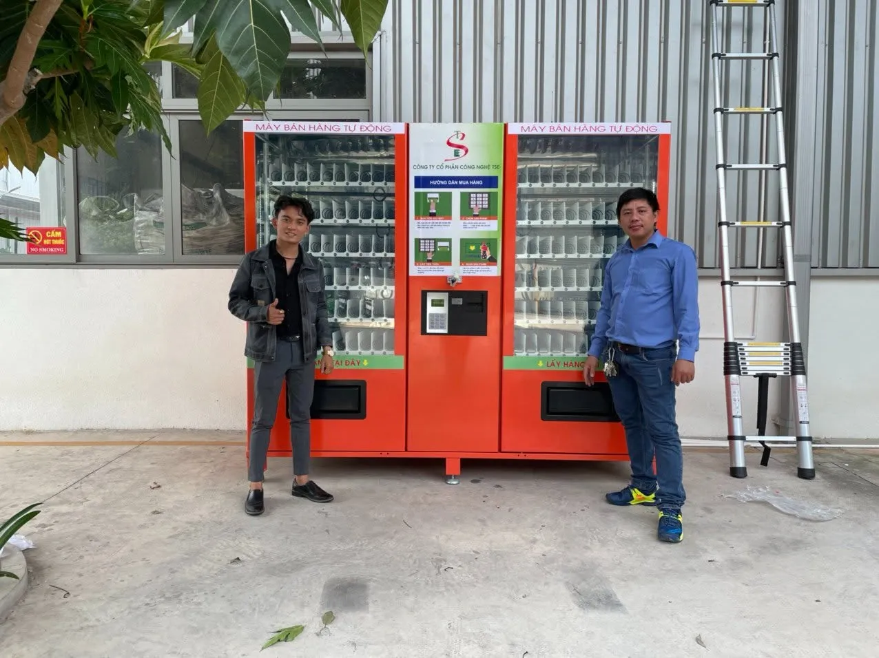 Hai đại diện giơ ngón tay cái hài lòng bên cạnh cụm máy đôi bán hàng tự động vừa bàn giao