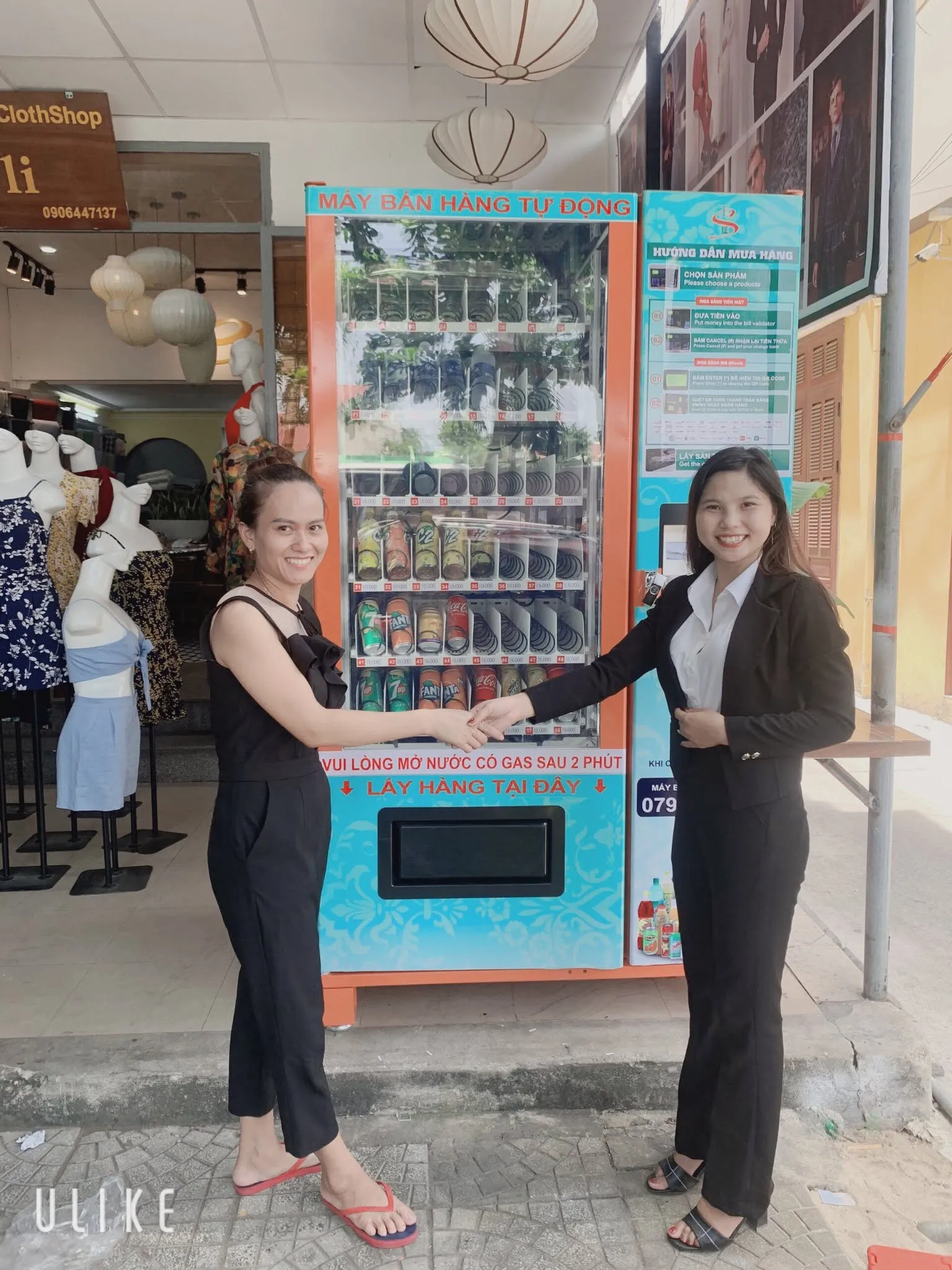 Đại diện TSE bắt tay khách hàng nữ nhận máy bán hàng tự động đặt trước cửa hàng thời trang