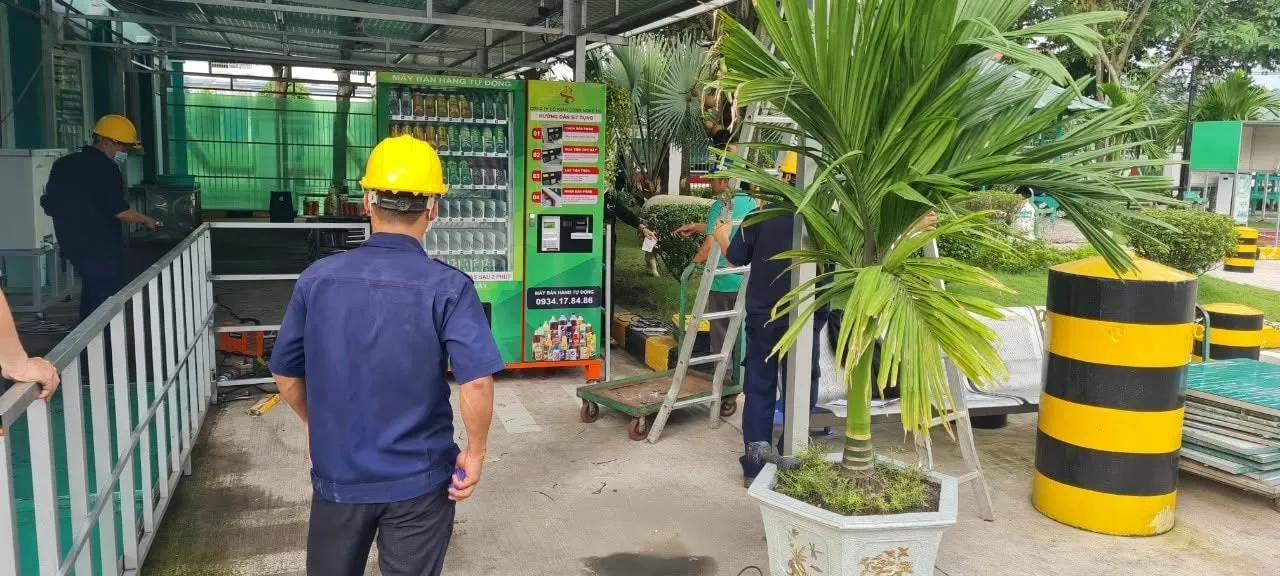 Máy bán hàng tự động đang được lắp đặt tại khu vực cây xăng, công nhân đội mũ bảo hộ thi công