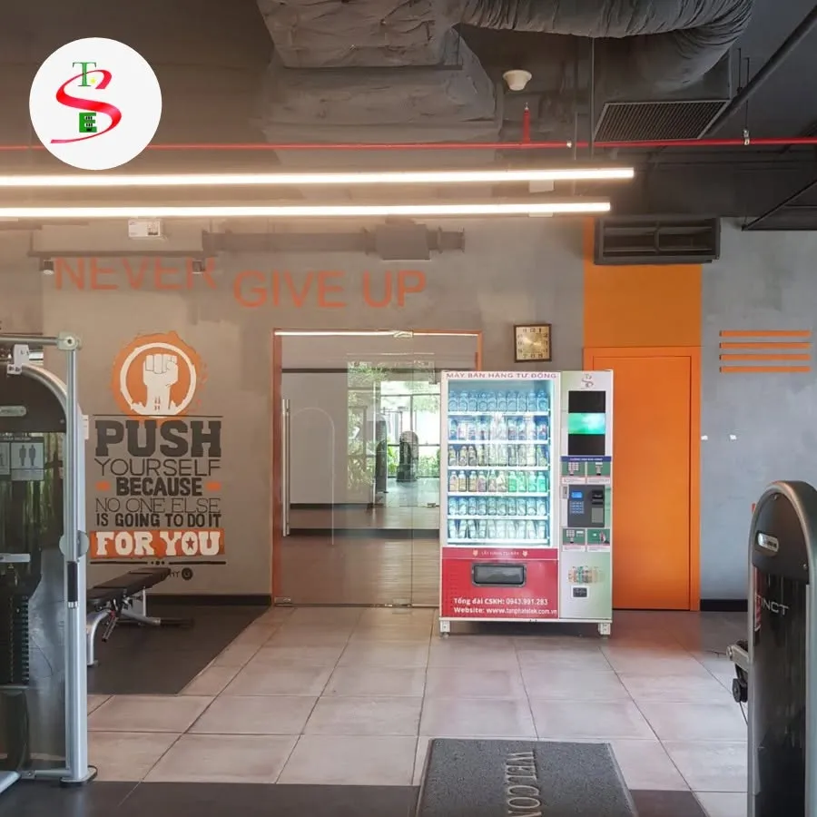 Máy bán nước tự động đặt trong phòng tập gym, tường có dòng chữ động lực Never Give Up, Push Yourself