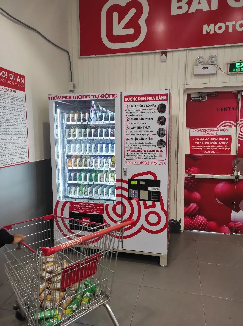 Máy bán hàng tự động đặt trong siêu thị bán lẻ, có xe đẩy hàng và bảng hướng dẫn mua hàng