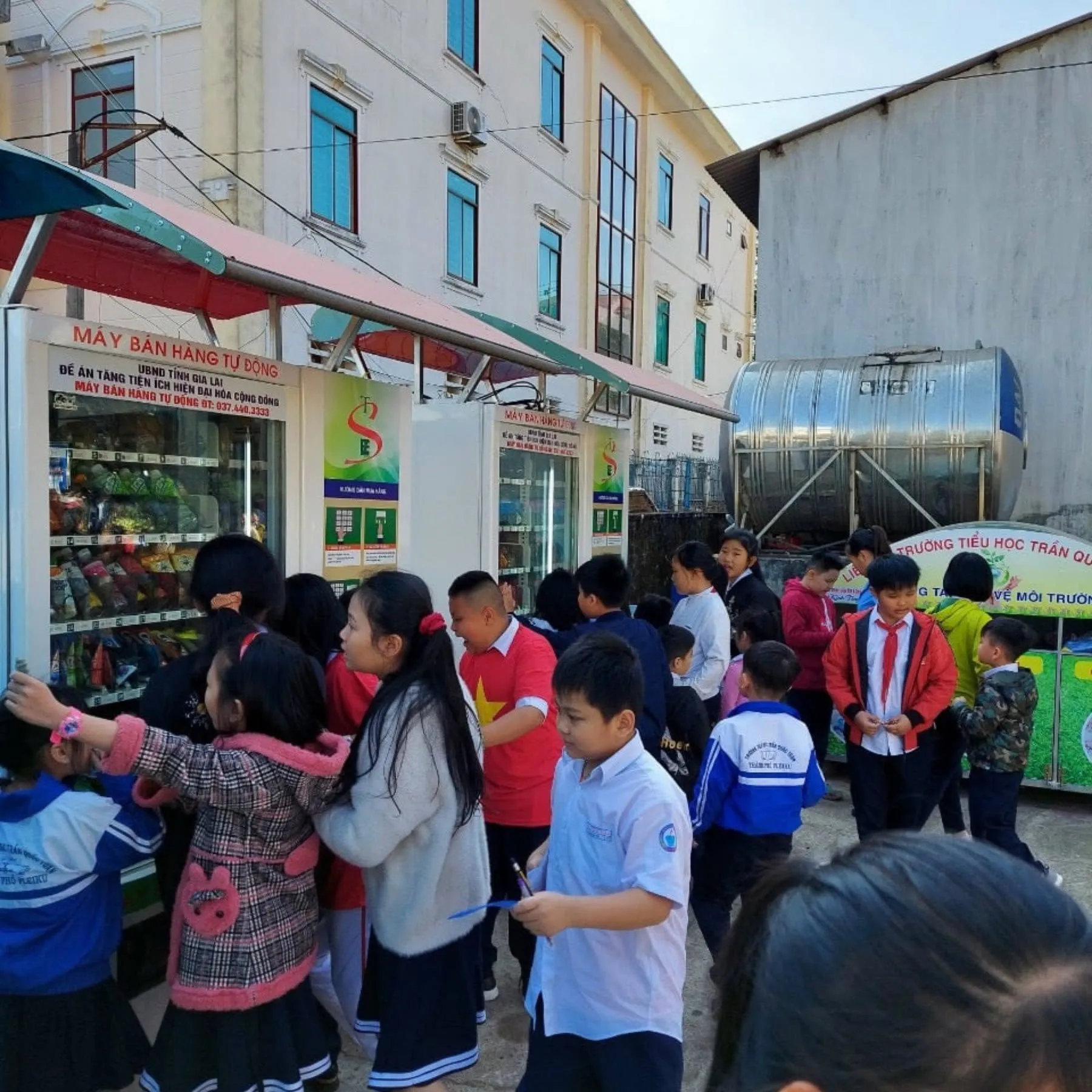 Đông học sinh tiểu học vây quanh máy bán snack tự động đặt trước cổng trường