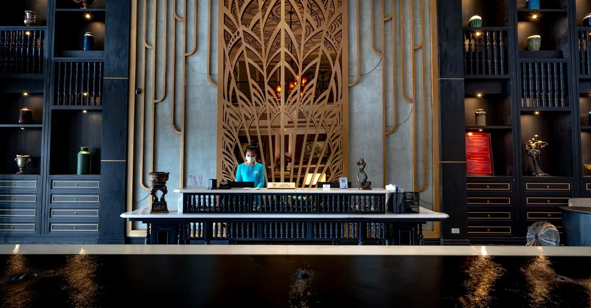 A woman speaks to a receptionist wearing a mask at a hotel reception.