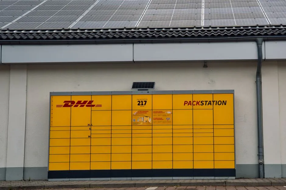 Yellow DHL Packstation under solar panels in Berlin, Germany, showcasing sustainable technology.