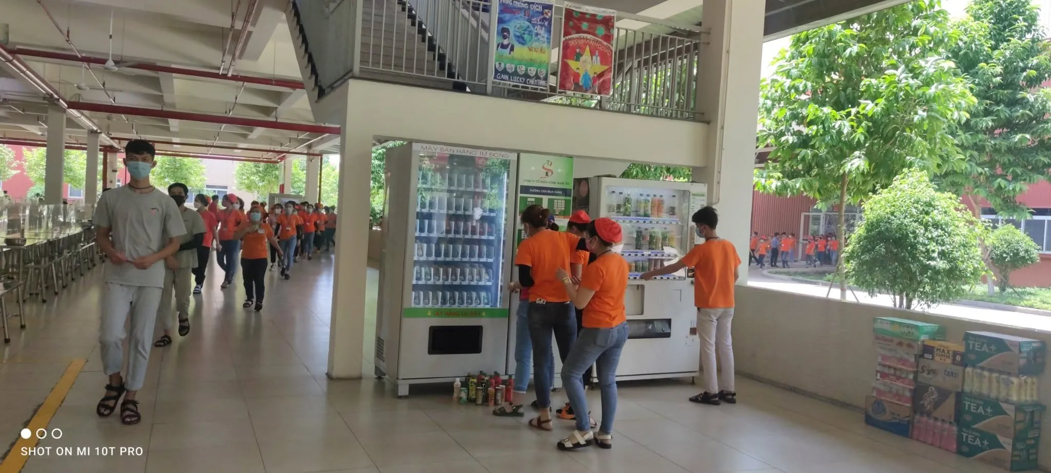 Nhân viên châm hàng cho hai máy bán hàng tự động đặt cạnh nhau trên phố, hàng hóa xếp dưới đất chờ nạp